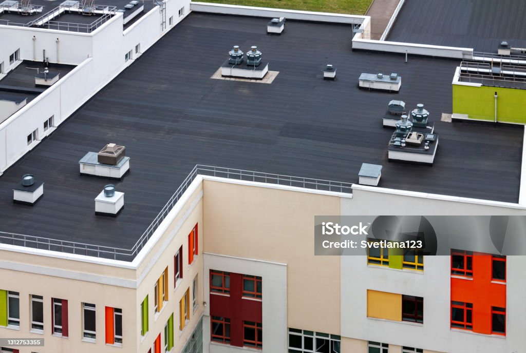 Top view dark flat roof with air conditioners and hydro insulation membranes modern apartment building residential area. Top view flat roof with air conditioners and hydro insulation membranes on top of a modern apartment yellow green red building. Rooftop Stock Photo