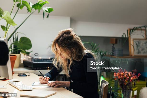 Young Caucasian Female Professional Working From Home Sitting In Her Office Area And Writing Notes Stock Photo - Download Image Now