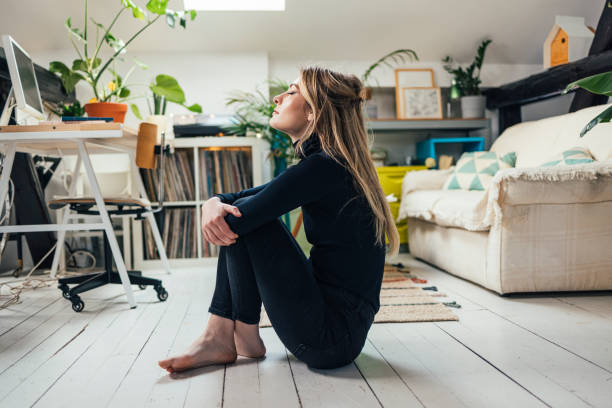 Horizontal side view shot of a beautiful blond woman dressed in black, sitting on a floor in the middle of a bright living room, practicing breathing with her eyes closed (copy space)