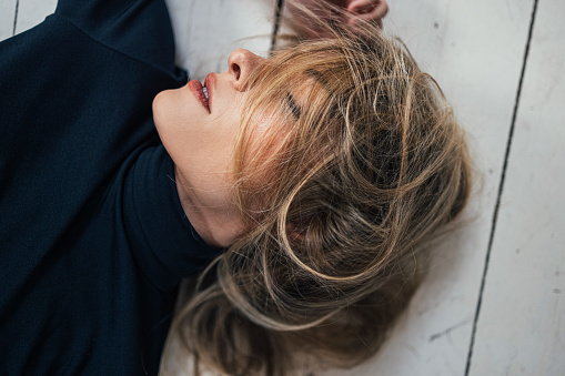 Close up shot of a tired young woman lying on a white wooden floor with messy hair and her eyes closed ( horizontal)