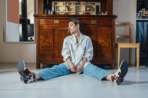 Beautiful fashionable young woman in white shirt and ripped jeans, leaning against antique peace of furniture, looking on the side, feeling sadtiredindifferent ( copy space)