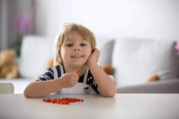 Photo of Cute little child, toddler boy, eating alfa omega 3 child supplement vitamin pills at home