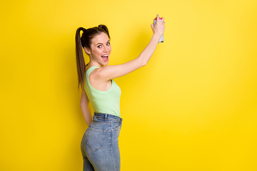 Photo of young woman hold spray paint can draw wall good mood isolated on bright shine yellow color background.