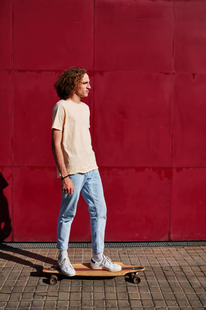 istock a young man with curly hair using his skateboard with a red background behind him on a sunny day 1312756814
