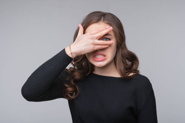 istock Worried, scared young woman looking between fingers, isolated over gray background. Half length portrait 1312760136