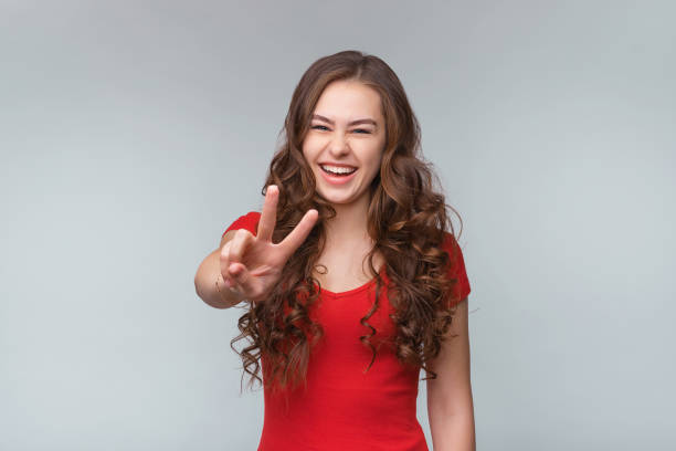istock Cheerful young woman with positive expression showing victory or peace gesture, standing against gray background 1312760142