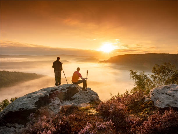 dos fotógrafos en la cima de una colina en el trípode de la cámara de búsqueda de objeto de composición al atardecer. hombre tomar foto - rock climbing fotos fotografías e imágenes de stock