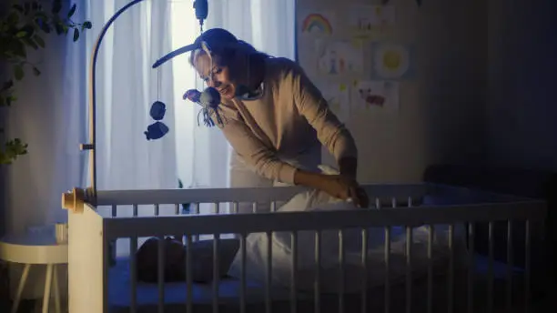 Photo of Authentic Shot of a Mother Soothing and Cuddling a Newborn Baby Boy in Child Crib. Caucasian Neonate Toddler at Home in Kids Bedroom. Concept of Childhood, New Llife and Parenthood.