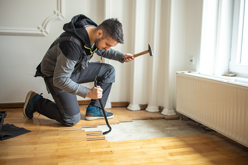 Manual worker removing parquet flooring during home renovation