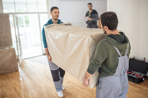 Professional movers carrying in new furniture, that's in cardboard box, in house