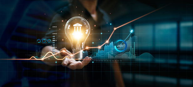 Businessman holding creative light bulb with growth graph and banking icons. Financial innovation technology develop new products and services that enhance successful and profit in global business.