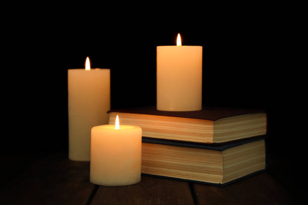 istock Burning candles and stack of books on wooden table in darkness 1312770143