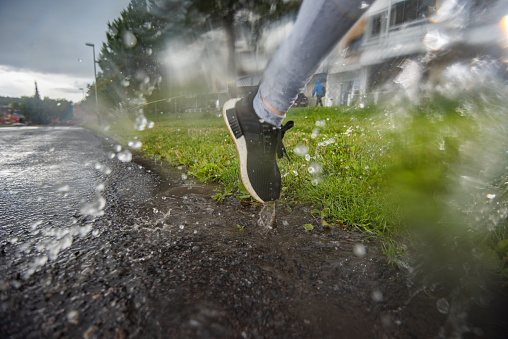 Unrecognizable athletic woman running on the road during rainy day