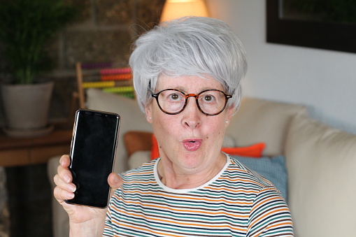 Senior woman showing telephone screen at home.