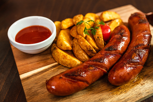 Sausages and baked potato served on wooden board