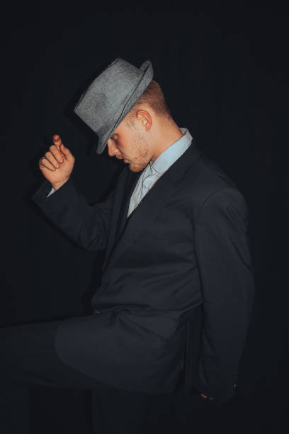 Young man wearing black suit and hat posing on black background