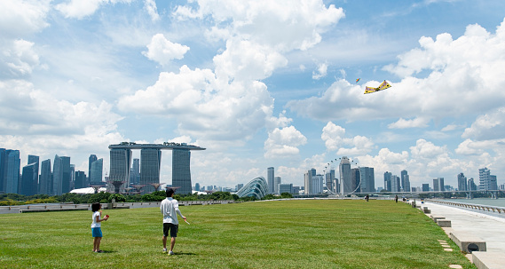 Singapore, October 2019: People playing and flying kites on grass at Marina Barrage recreational park. Singapore city skyline with Marina Bay Sands hotel, city downtown and modern skyscrapers