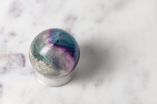 This is a photograph of a crystal ball made from green and purple fluorite on a white marble table top background.