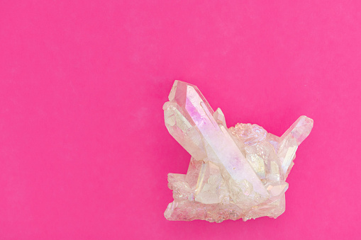 This is a photograph of a cluster of angel aura quartz points on a pink background. Angel Aura Quartz is made by coating crystals, such as quartz, with metal to give them an iridescent metallic sheen. The Angel Aura Quartz signifies hope, joy, and optimism.