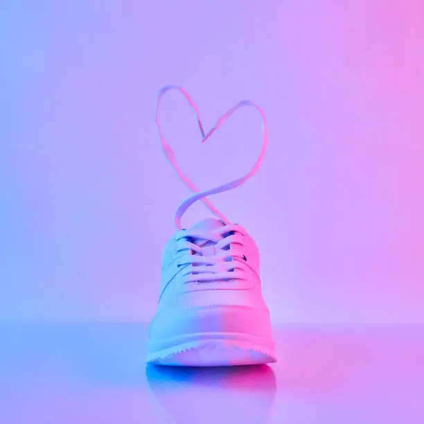 Sports sneakers with heart-shaped laces in neon light. Concept of Love and Valentine's Day.