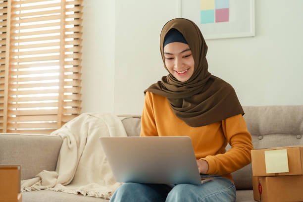 Muslim young women wear hijab using typing and checking order the customer address on the computer laptop at home morning. Concept business small and shop online stock photo
