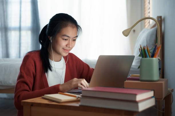 Asian woman video call online via the internet tutor on a computer laptop with headphone, Asia girl is studying while sitting in the bedroom at night. Concept online learning at home stock photo