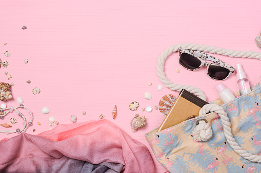 Beach bag, moisturizers, sunglasses, seashells on a pink background, flat lay.Summer travel holiday vacation background, sunbathing accessories