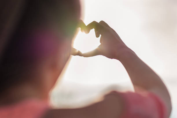 istock Woman making heart shape with hands against sky in sunlight 1312819702