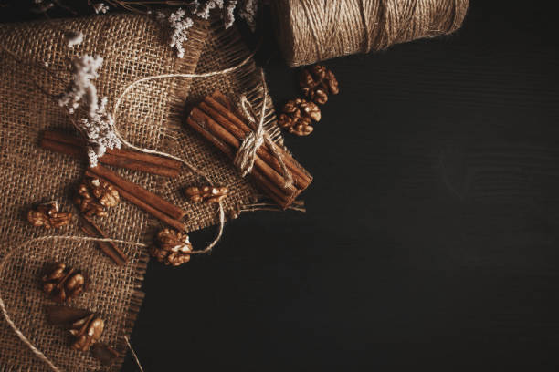 Still life on a black wooden background. Cinnamon and walnut on a burlap cloth. Roll of twine. Cinnamon rewound thread.