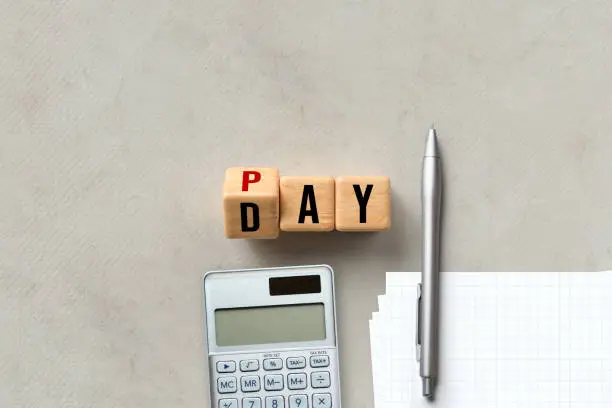 Photo of Pay Day concept with alphabet letters on wooden blocks, calculator and pen