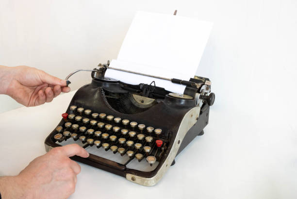 istock An old typewriter and a blank sheet of paper inserted. Isolated on a white background. The hands of the master set up the typewriter 1312828148