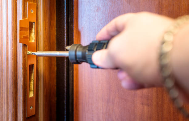 a man drives a screw into a door lock with a screwdriver stock photo