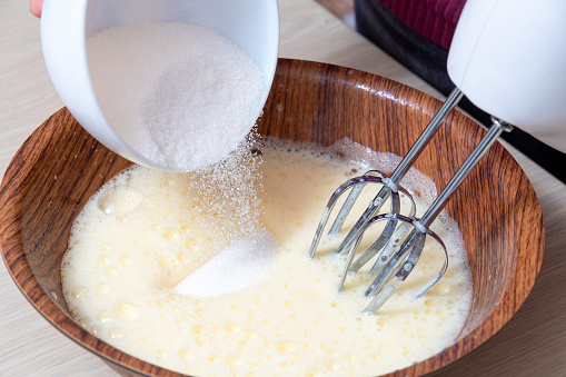 Adding sugar in the process of beating eggs with an electric mixer. The cooking process. Selective focus.