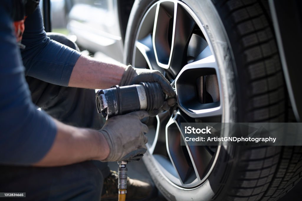 Tire changing in a car service Close-up shot of an unrecognizable auto repairman changing whleel and tire in a workshop. Tire - Vehicle Part Stock Photo