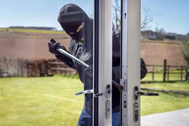 Burglar or thief breaking into a home through window with a crowbar