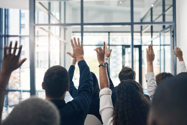 Shot of a group of businesspeople raising their hands during a presentation stock photo