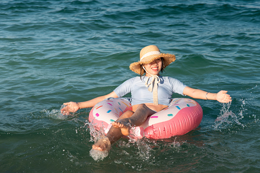 Woman swimming and floating on the seaside water with doughnut float on a sunny day. Summer vacation and leisure abstract