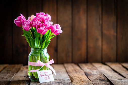 Front view of pink tulips bouquet in a glass jar and a greeting card with the text 