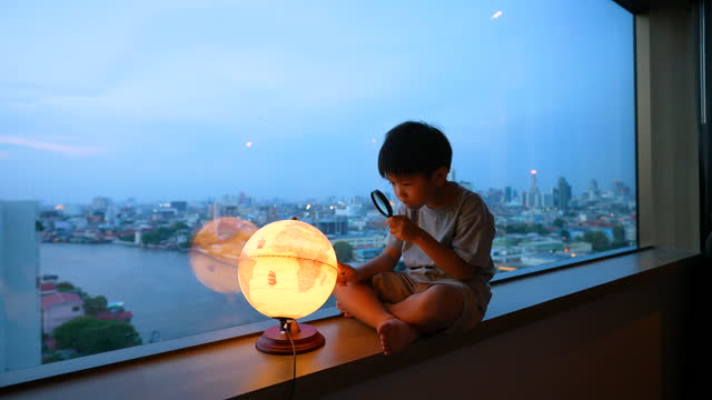 Kid learn about the globe with glass magnifier at skyscraper. Concept self-learning and environment