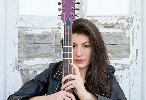 Winsome Caucasian Female Guitar Player With White Bass Guitar Holding Instrument Nearby With Positive Expression Over Trendy Turquoise Background. Horizontal Image Composition