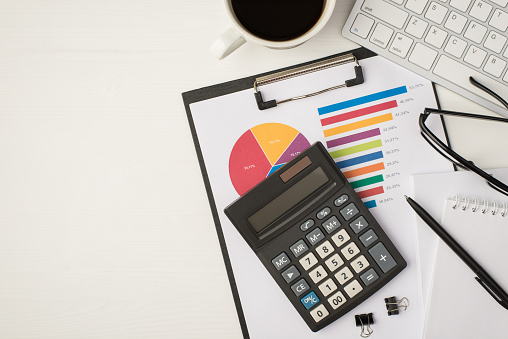 Top view photo of business workplace with keyboard glasses binders pen notebook cup of coffee and calculator on pie chart diagram on isolated white background with copyspace