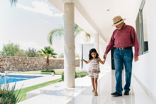 Grandfather and granddaughter walking by the hand on the poolside of a Holiday Villa