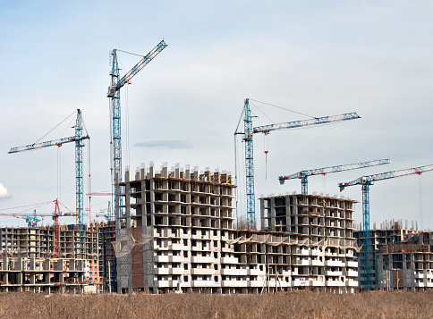 Construction site with multi-storey buildings and cranes at cloudy sky background