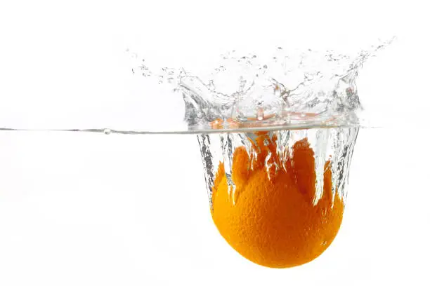 Photo of one ripe juicy orange falls into the water with splashes on a white background