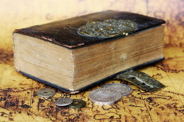 Old silver coins from 1902 and an antique book from 1763 on a world map