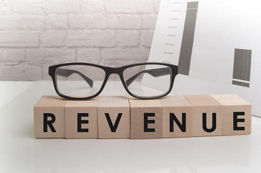 Word Revenue on ascending arrow above bar graph of Wooden small cubes isolated on black background. Chalk drawing on blackboard. Business Concept image.