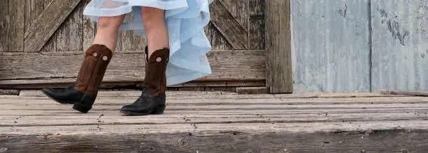 Cowboy boots on a teen girl's feet in a rustic Western setting. Web banner crop.