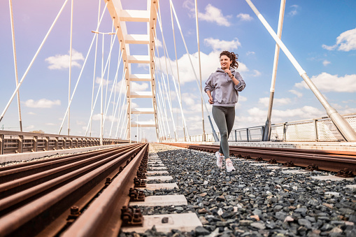 Full length photo of sporty young woman running next to train tracks on the bridge.