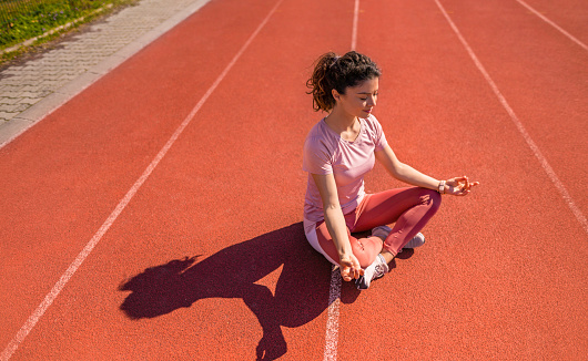 Photo of young female athlete meditating on sports track. Vibrant colors and very high resolution. Springtime.