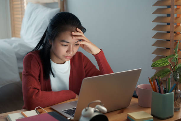 Asian girls are sitting bore online with a tutor on a laptop while sitting in the bedroom at home night. Concept online learning at home stock photo